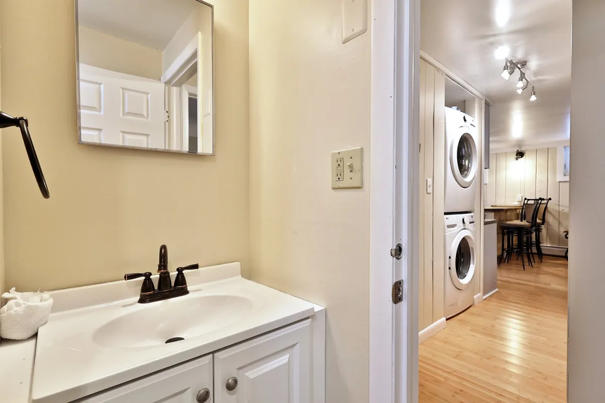 A practical, well-lit corner showing laundry machines, a sink with a clean faucet, a mirror, and a glimpse of a dining area. The atmosphere is both functional and inviting, emphasizing convenience and ease for active travelers.
