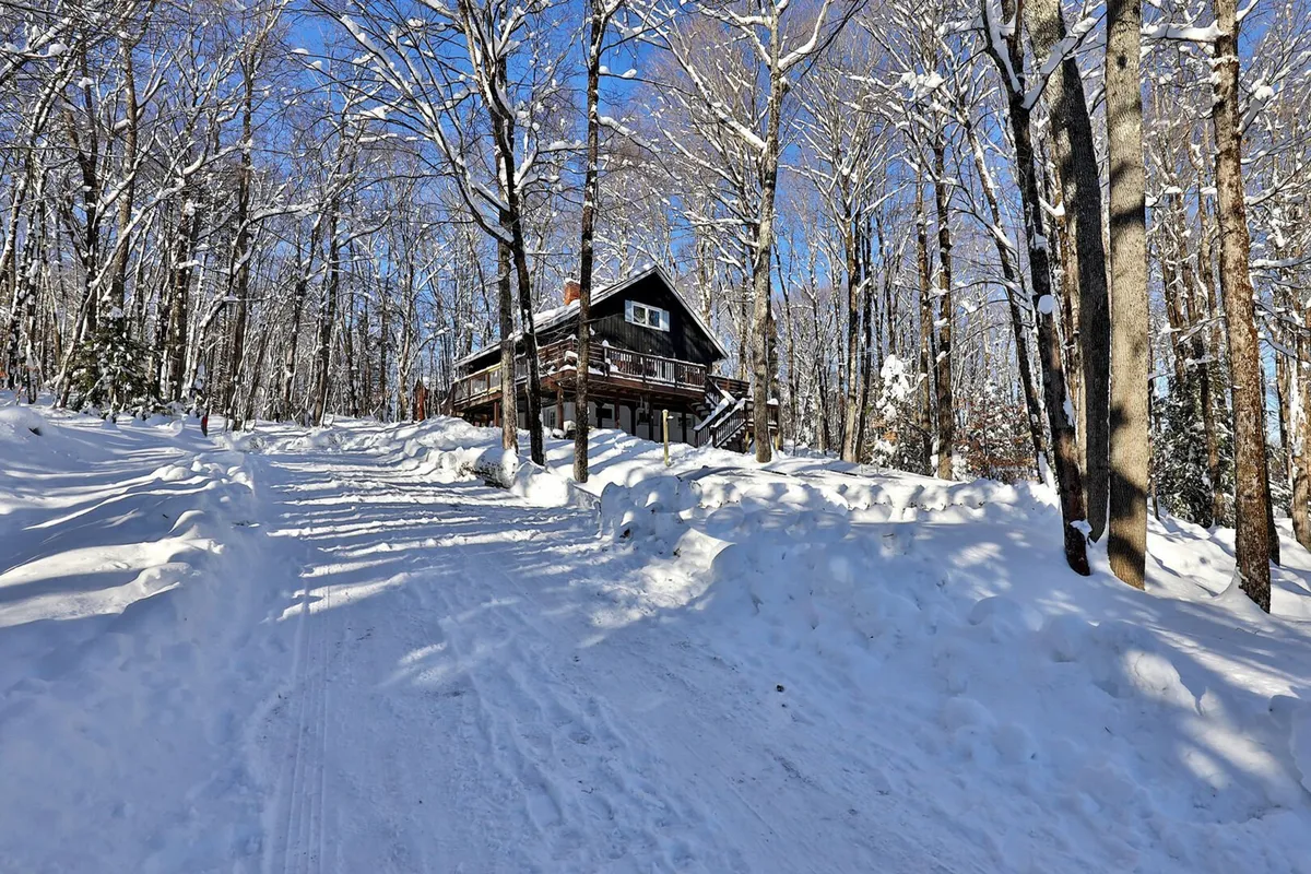 A snow-covered pathway leads to a wooden cabin surrounded by bare trees, evoking a serene winter setting. The environment is inviting for snowy adventures like cross-country skiing, snowshoeing, and post-activity relaxation. The image embodies the Vermont winter experience mentioned in the section.