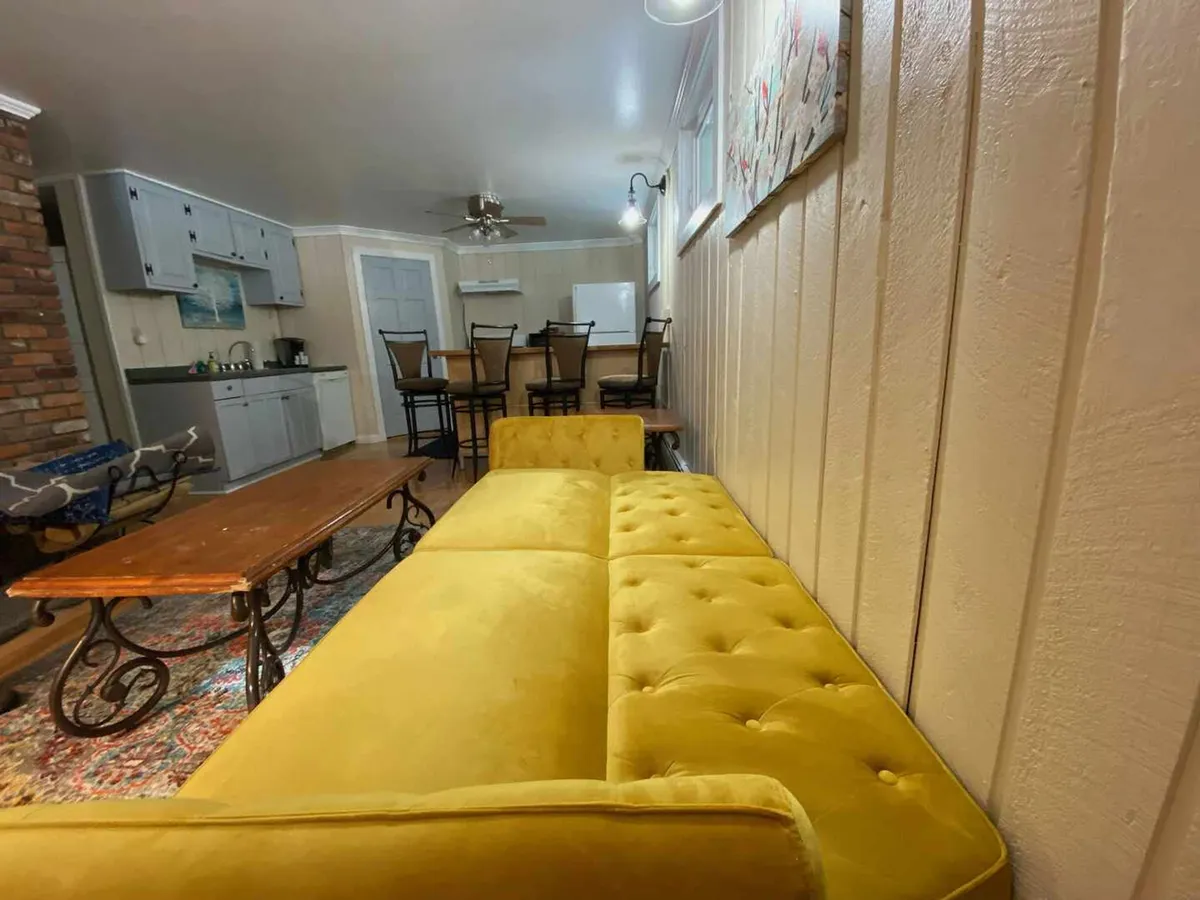 Bright, cheerful living area featuring a yellow tufted sofa, a wooden coffee table, and a brick wall. The layout encourages conversation and casual dining, ideal for gathering with friends before or after a night out.