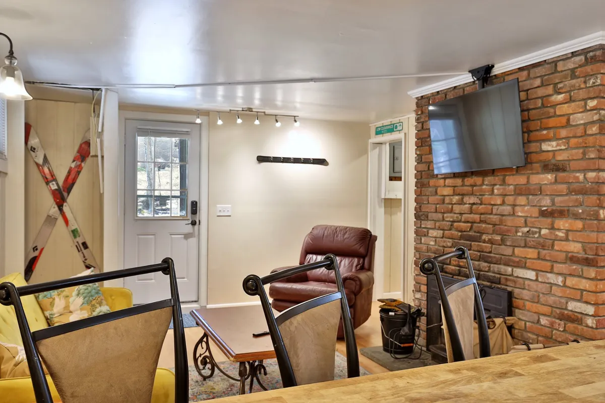 A view of the living area with a yellow sofa, brick wall, recliner chair, coffee table, and a television. The room exudes coziness, inviting guests to relax, watch TV, or enjoy snacks after a day outdoors.