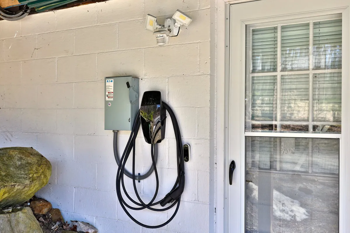 This exterior image prominently features the electric vehicle charging station situated beside a power supply box and a distinctive stone feature, with a practical, modern vibe. The area is well-lit and clearly marked, making it easy for guests to identify where to charge their EVs upon arrival.