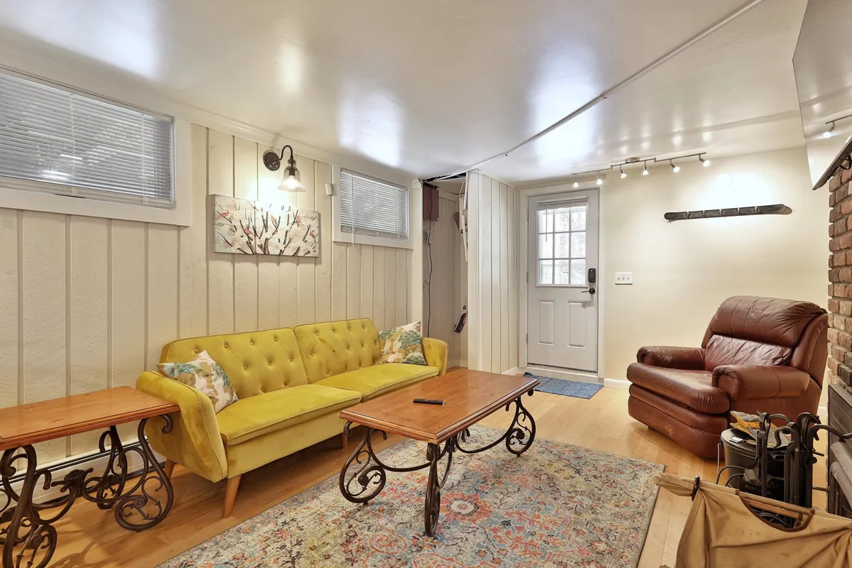 A warmly lit living room with a yellow sofa, wooden coffee table, and a brick feature wall. The space feels inviting, with spots for relaxing, socializing, and enjoying TV after a night out.