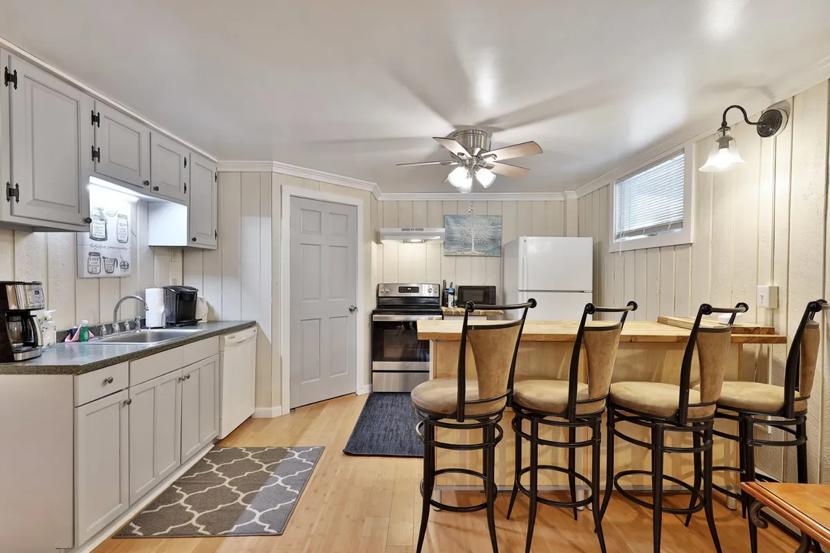 This image showcases a spacious kitchen featuring a central island with seating and sleek stainless steel appliances. The setting is bright and open, ideal for both meal preparation and socializing. Modern light fixtures add warmth and style to the space, making it inviting for cooking and gathering.